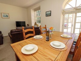 A dining area with a wooden table set for four, a television in the background, and a window with a view of the outdoors.
