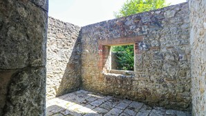 Um quarto com paredes de pedra, uma pequena janela e soalho de pedra.