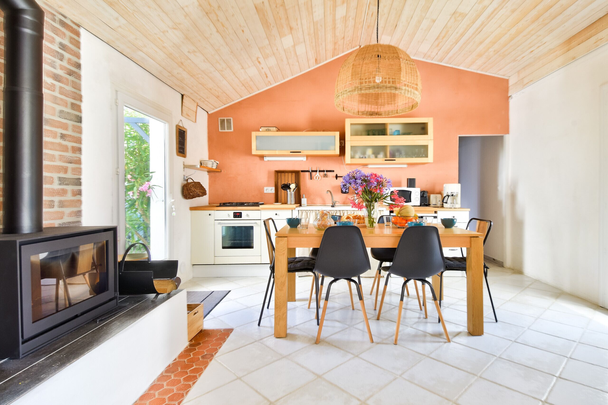 A modern kitchen with a large island, wooden ceiling, and a hanging light fixture.