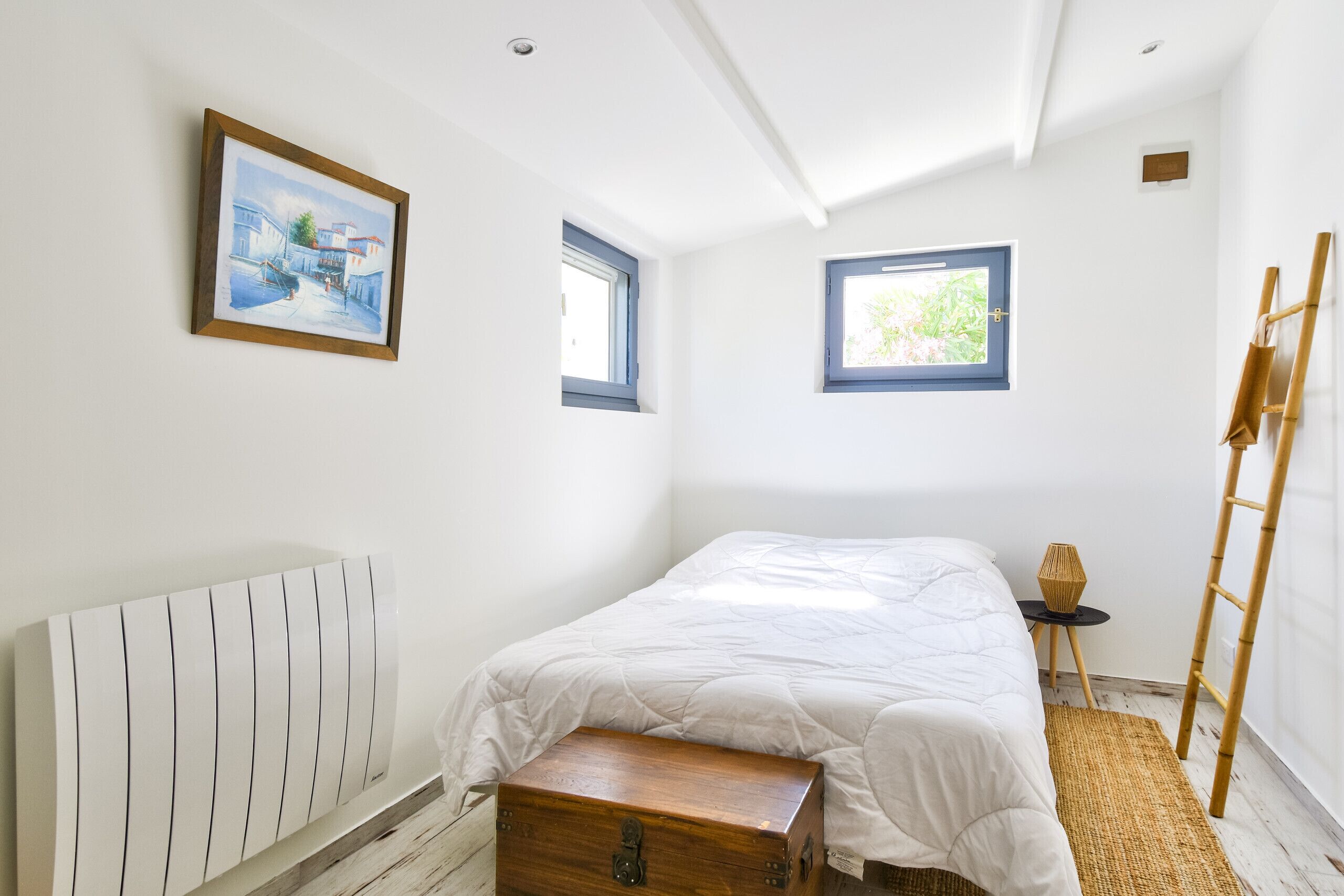 Una camera da letto con un letto, un baule in legno, un termosifone, una finestra e un quadro appeso al muro.