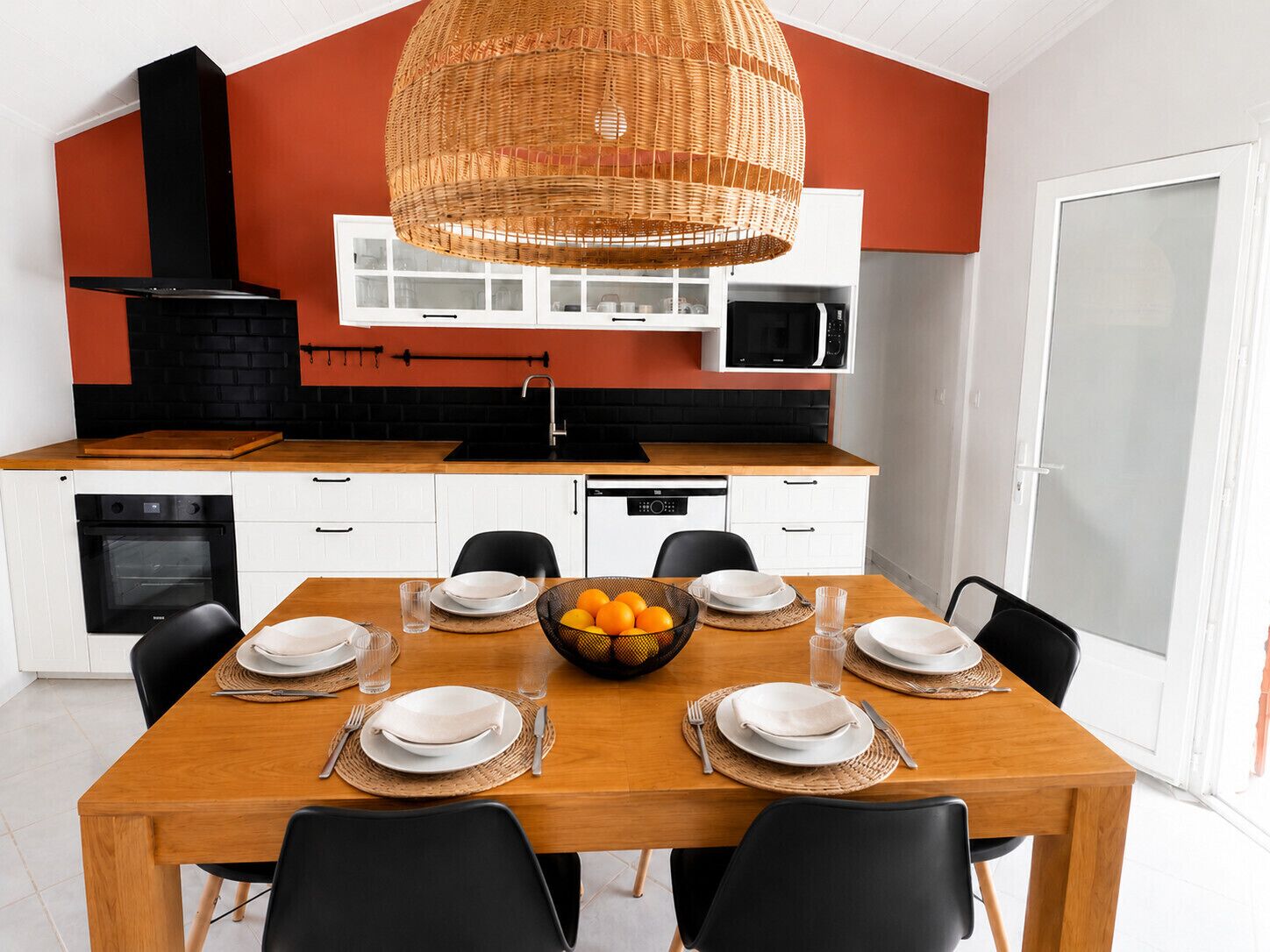 Una cocina moderna con armarios blancos, un microondas negro y una mesa de comedor de madera preparada para cuatro comensales.