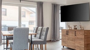 A modern living room with a flat-screen TV, grey upholstered chairs, a wooden cabinet, and a dining area with a table and chairs. - Holiday Apartment in St. Englmar (Sankt Englmar)
