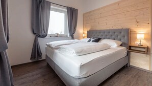 A bedroom with a large bed, grey curtains, a wooden headboard, and bedside lamps. - Holiday Apartment in St. Englmar (Sankt Englmar)