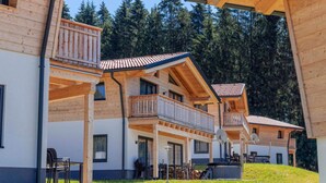 A wooden chalet with multiple balconies, large windows, and a view of a forested mountain. - Holiday Apartment in St. Englmar (Sankt Englmar)