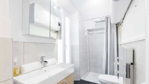 Moderni kylpyhuone, jossa on valkoinen pesuallas, peili, suihku ja wc.