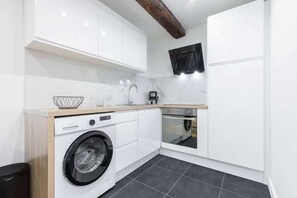 Una cocina compacta con muebles blancos, lavadora, microondas y horno integrado.