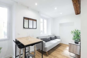 A modern, minimalist living space with a dining area, sofa, and a small side table with a plant.