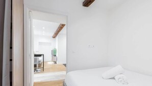 Ein Schlafzimmer mit einem Bett, Holzboden, einer weißen Wand und einer Tür zu einem Badezimmer.
