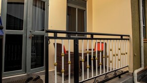 Een balkon met rieten meubilair, een zwarte metalen balustrade en een deur met glaspanelen.