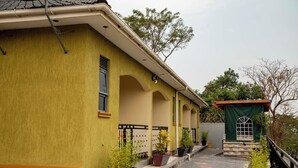 Een geel gebouw met een overdekte veranda, bloempotten en een kleine tuin.