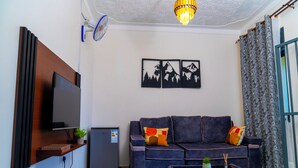 Een woonkamer met een flatscreen televisie, een bank, een salontafel, een kleine koelkast en een plafondventilator.