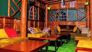 Een rustiek houten interieur met een vloer van kunstgras in groen, houten meubels en een raam met een kruisverbinding.
