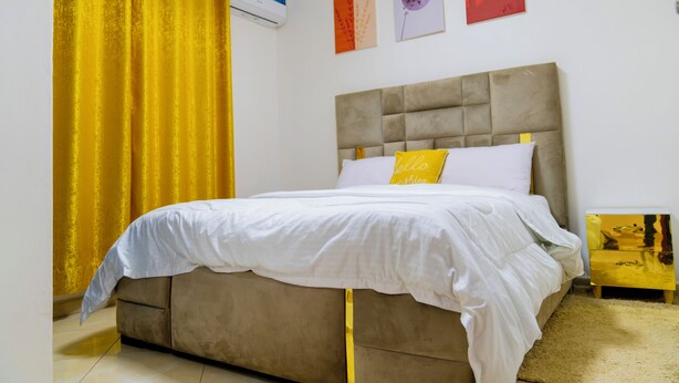 Een slaapkamer met een bed, een nachtkastje, een geel gordijn en wanddecoratie.