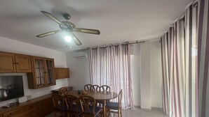 A dining area with a round table and chairs, wooden cabinets, a ceiling fan, and a TV.
