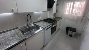 A compact kitchen with white cabinets, a stainless steel sink, a built-in oven, and a small trash bin.