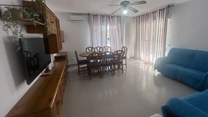 A living room with a TV, wooden furniture, a ceiling fan, and striped curtains.