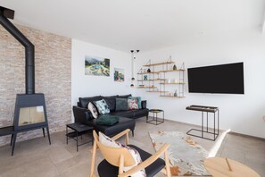 A modern living room with a fireplace, a black sofa, a wooden chair, a flat-screen TV, and a brick wall.