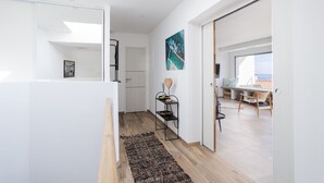 A modern interior with a hallway leading to a dining area, a black metal shelf with decorative items, and a large window offering a view. - Dream Vacation in a Beautiful Villa with Exceptional Sea View (Cerbère)