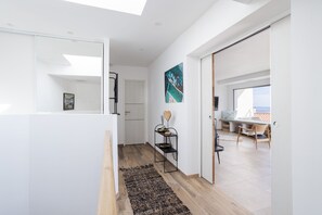 Un intérieur moderne avec un couloir menant à un espace repas, une étagère en métal noir agrémentée d’objets décoratifs et une grande fenêtre offrant une vue dégagée.