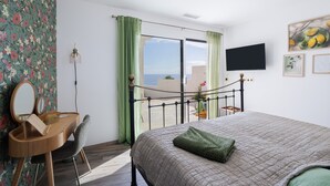 A bedroom with a bed, a desk with a mirror, a TV, and a view of the outdoors. - Dream Vacation in a Beautiful Villa with Exceptional Sea View (Cerbère)