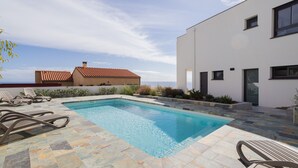 A swimming pool with lounge chairs, a modern building, and a clear sky. - Dream Vacation in a Beautiful Villa with Exceptional Sea View (Cerbère)