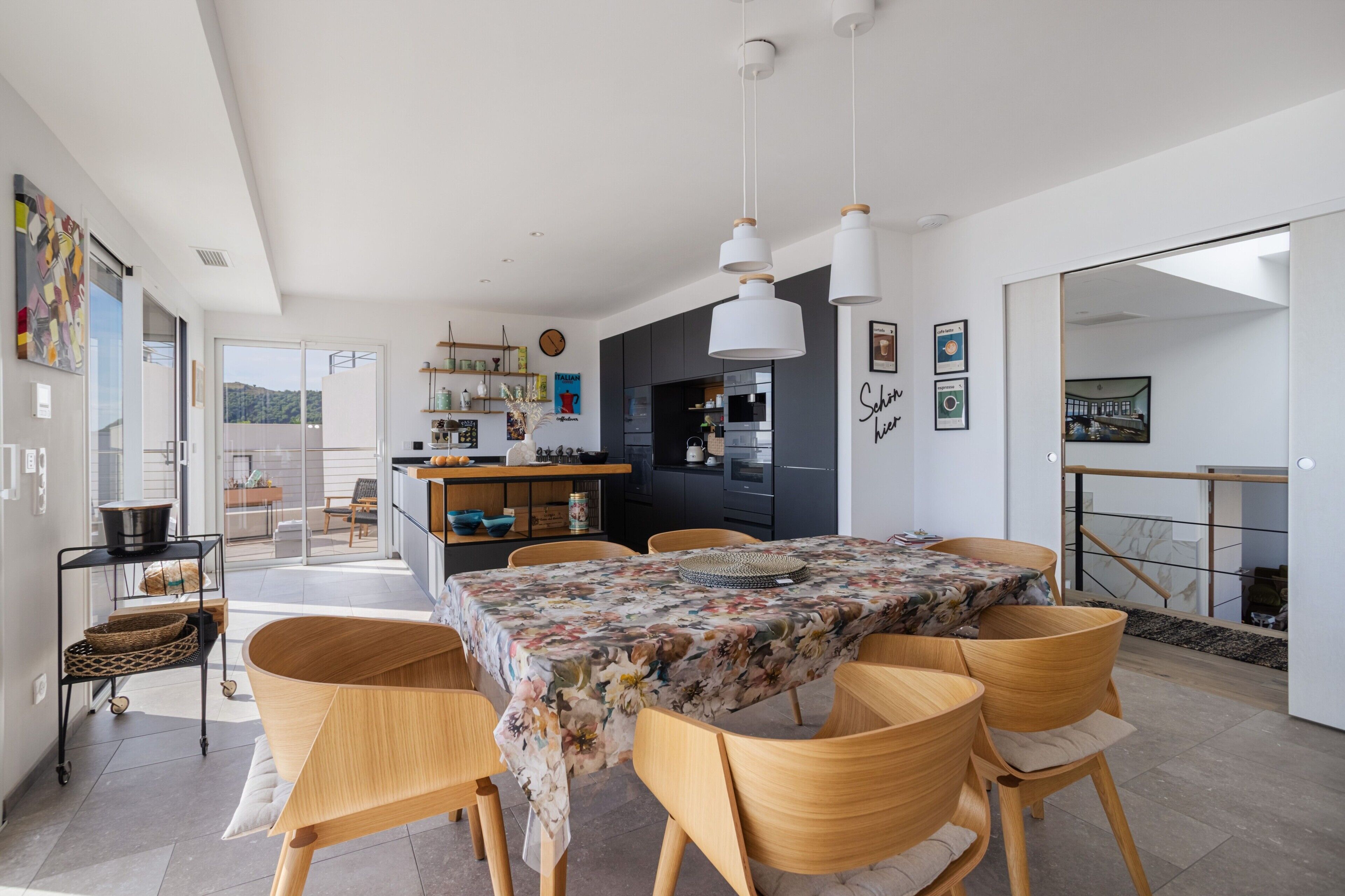 A modern kitchen with dark cabinets, a dining area with a floral tablecloth, and a view of the outdoors.