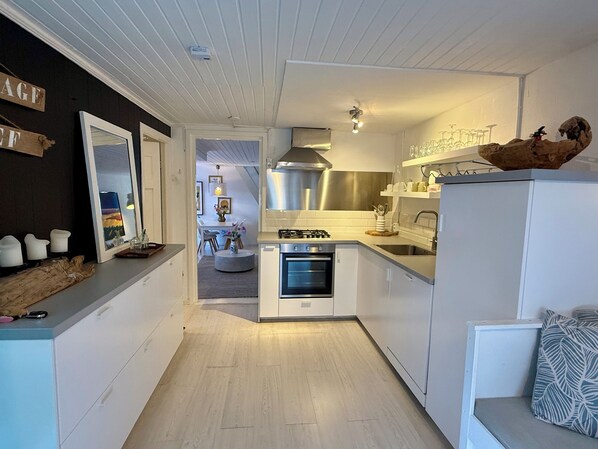 A compact kitchen with white cabinets, a built-in oven, and a gas stove. There is a wooden shelf with kitchenware and a small seating area with a cushion. - Idyllic vacation home with a terrace in Bergen, just 250 m from downtown! (Bergen)