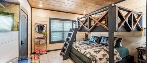 A bedroom with a four-poster bed, wooden flooring, a ladder, a desk with a computer, and a window with blinds.