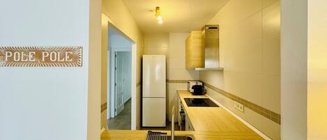 Cocina compacta con refrigerador, microondas y encimera de madera. Se ve un fregadero con un escurreplatos y un letrero que dice