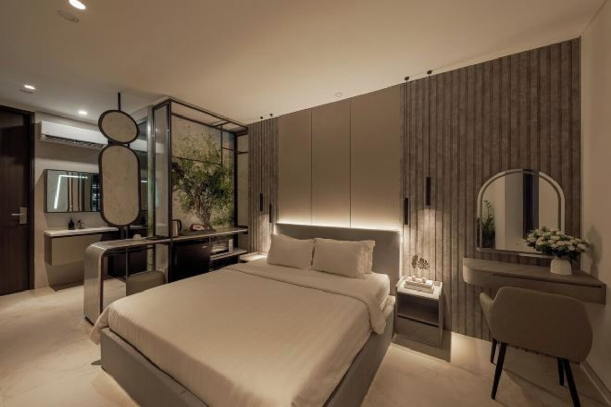 Een moderne slaapkamer met een groot bed, een bureau met stoel, een kaptafel met spiegel en een aan de muur bevestigde televisie.