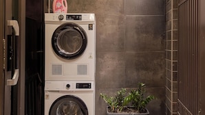A compact laundry area with stacked washers and dryers, a potted plant, and a wall-mounted light fixture.