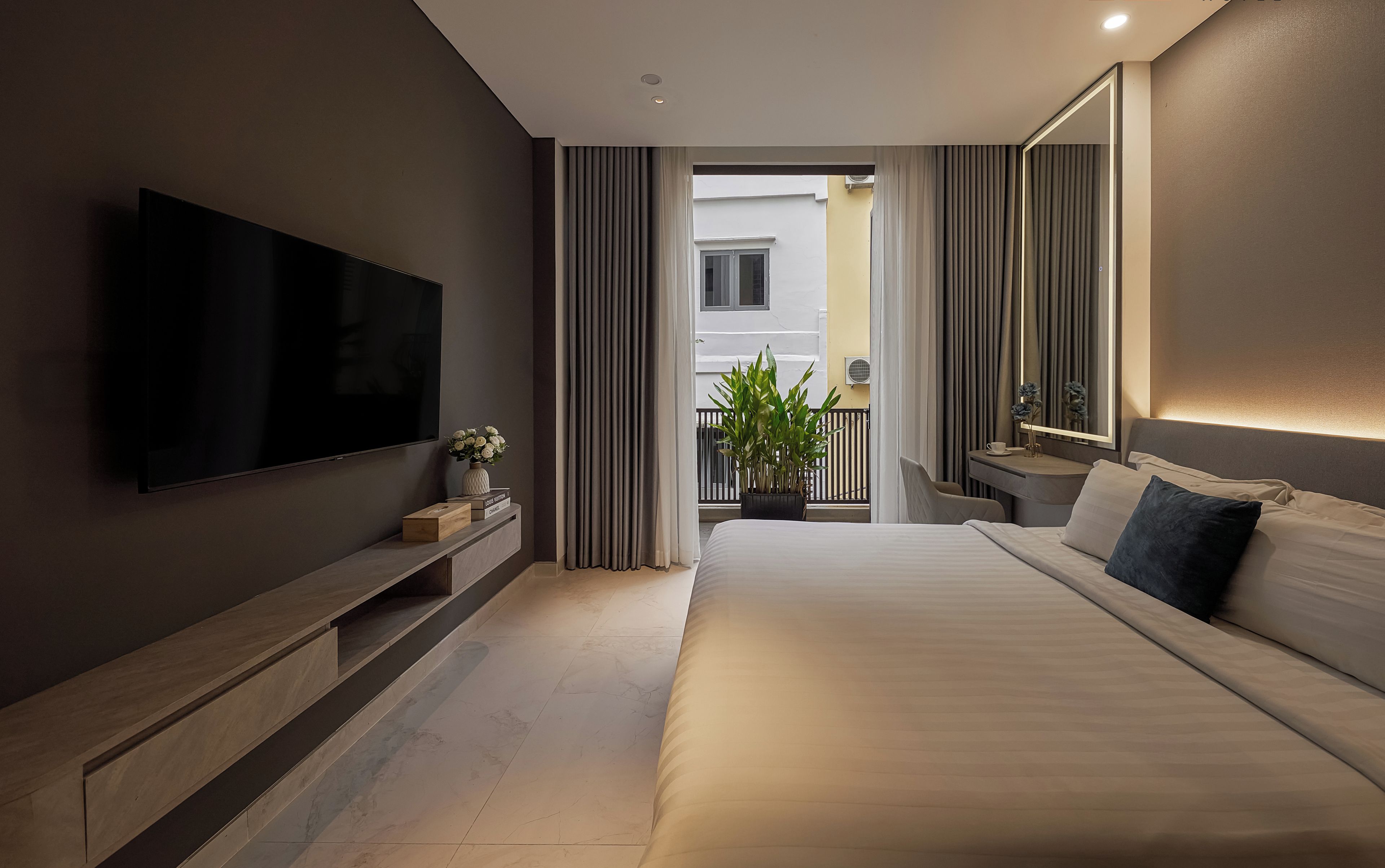 Moderni hotellihuone, jossa on suuri sänky, taulutelevisio, yöpöytä ja ruukkukasvi.