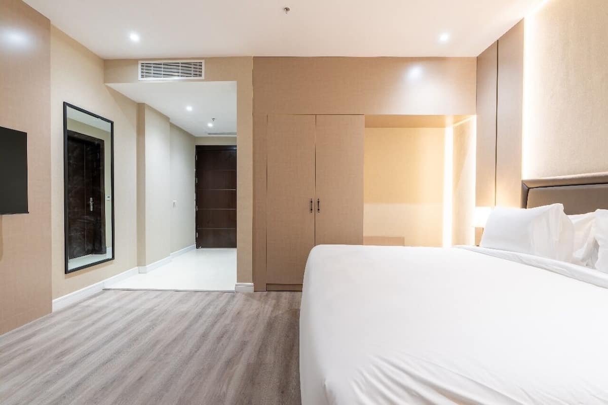 A hotel room with a large bed, a wardrobe, a mirror, and a door leading to a bathroom.