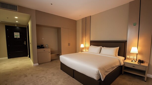 A hotel room with a large bed, bedside lamps, a wardrobe, and a desk with a lamp. - Towlan Al Rayan Hotel (Riyadh)