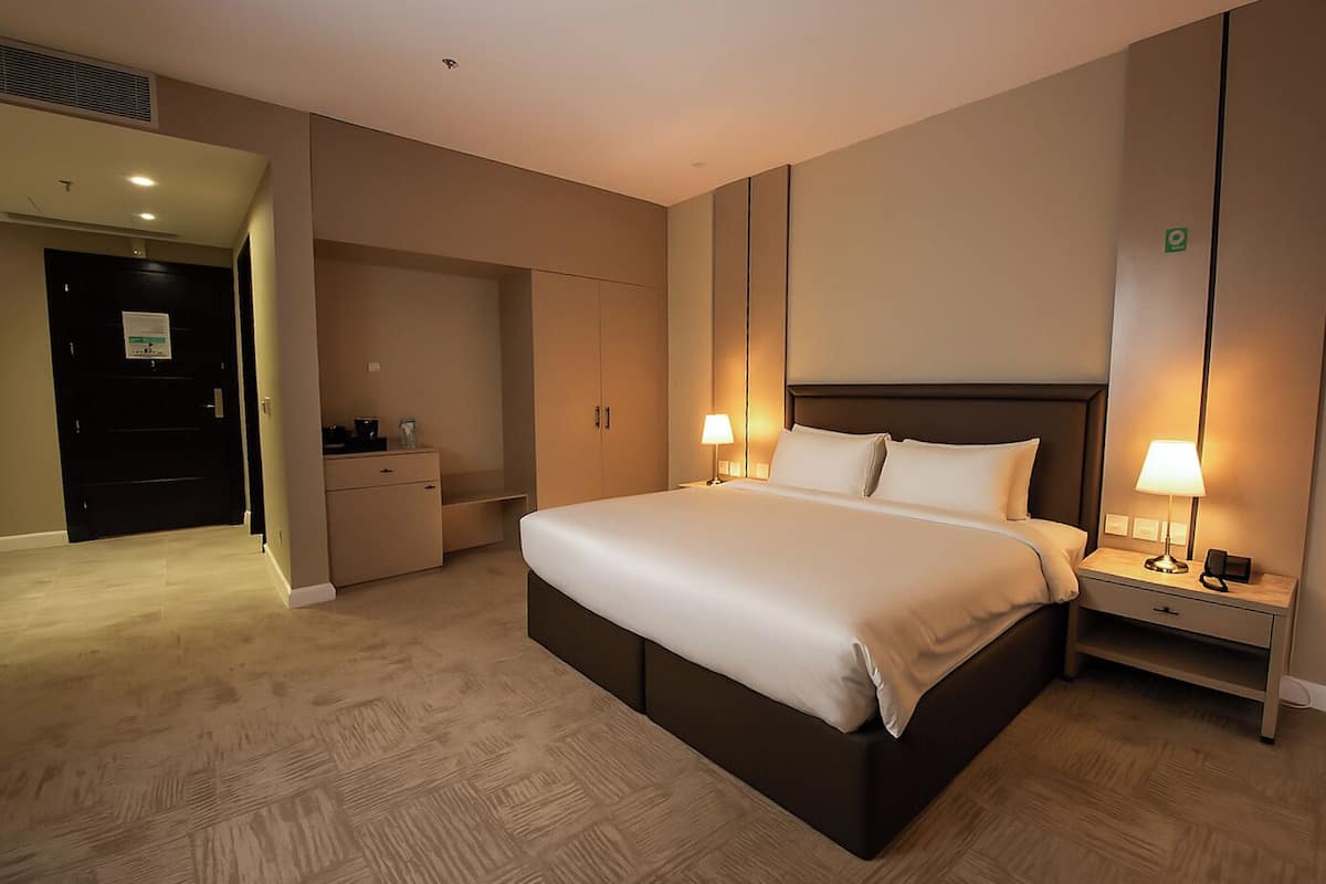 A hotel room with a large bed, bedside lamps, a wardrobe, and a desk with a lamp.
