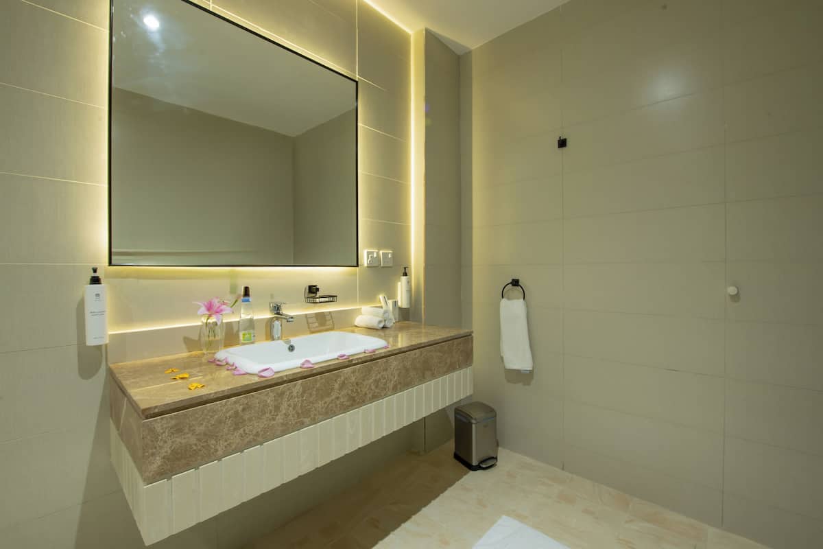 A modern bathroom with a large mirror, a sink with a marble countertop, and a trash bin.