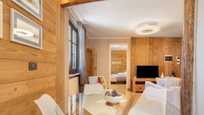Een moderne woonkamer met een glazen tafel, witte stoelen, houten wanden en een televisie.