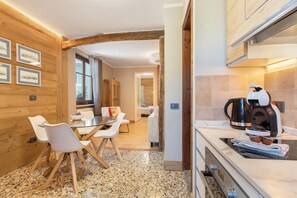 Une cuisine moderne équipée d’une machine à café, d’un coin repas avec des chaises et une table, de murs en bois et d’une vue sur une autre pièce.