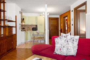 Un salon avec un canapé rouge, une table basse en bois et une cuisine en arrière-plan.