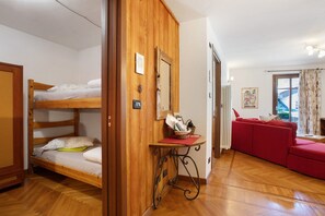 Une pièce avec un lit superposé, un canapé rouge, une petite table avec une lampe et une fenêtre avec des rideaux.