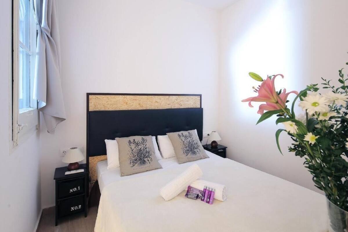 A neatly made bed with a headboard, two bedside tables, and a vase of flowers.