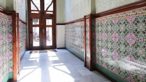 A hallway with ornate floral wall decorations, a wooden door at the end, and a tiled floor. - Hostal Balkonis (Barcelona)