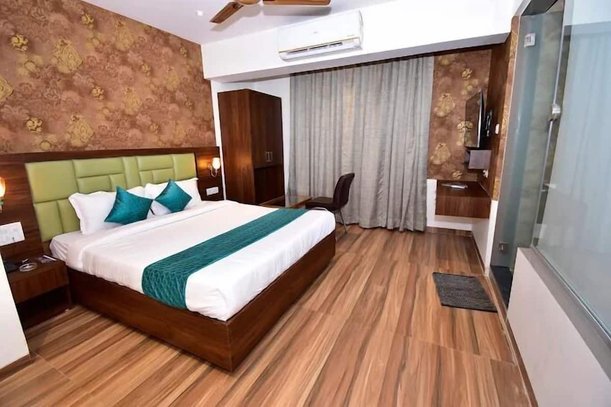 A hotel room with a large bed, a wooden headboard, a nightstand, a desk, a chair, and a large window with curtains.