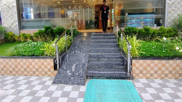 A hotel entrance with a glass facade, a staircase leading to the entrance, and a checkered floor pattern. - HOTEL CANDOR AMIGO (Panvel)