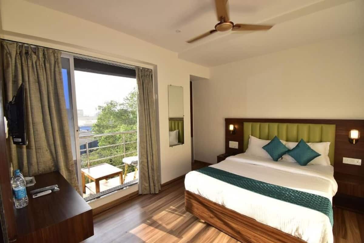 A hotel room with a bed, a desk, a chair, a ceiling fan, and a view of the outdoors.
