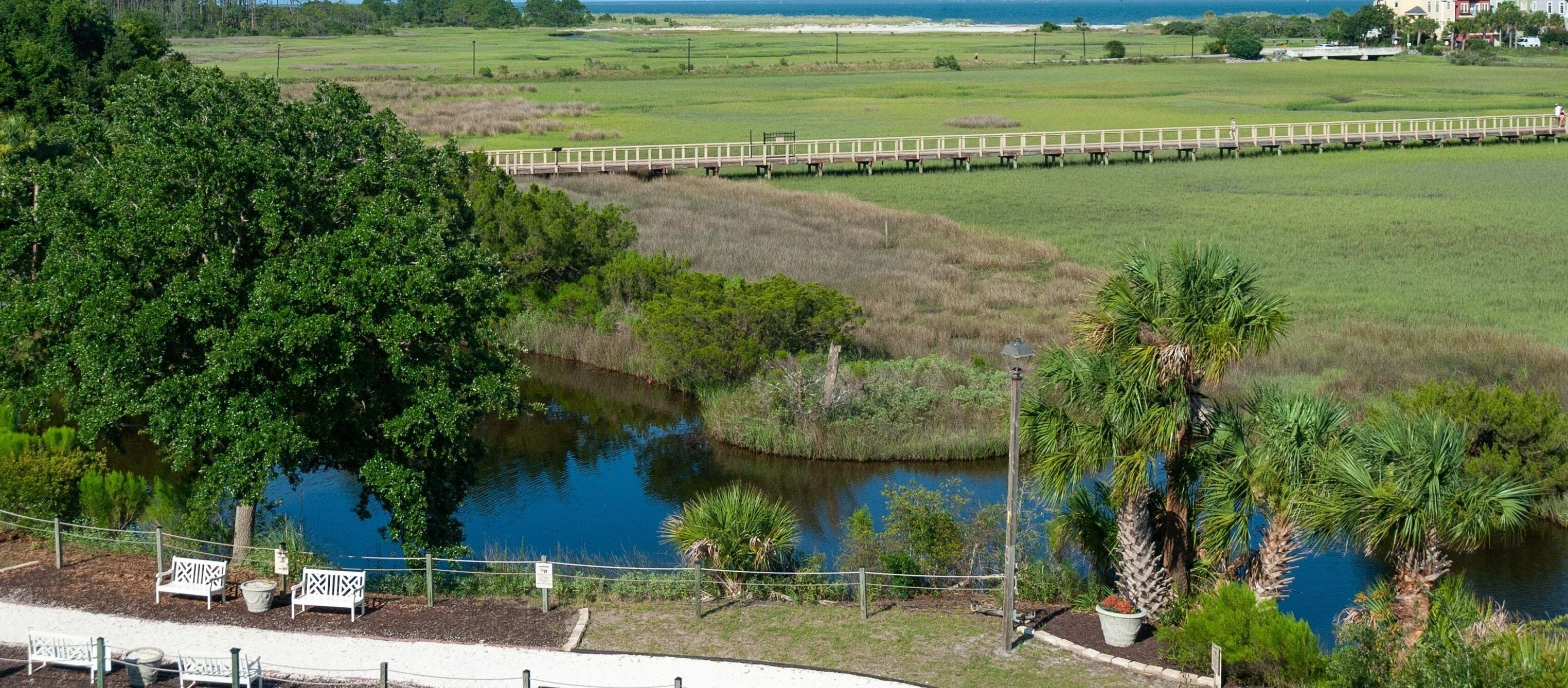 A view of a park with a walking path, benches, and a bridge over a pond.