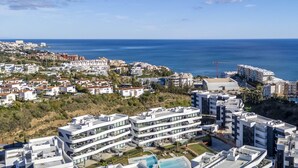 A coastal cityscape with modern buildings, a clear blue sky, and a view of the sea.