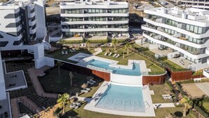 A modern hotel complex with multiple buildings, a central swimming pool, and outdoor seating areas.