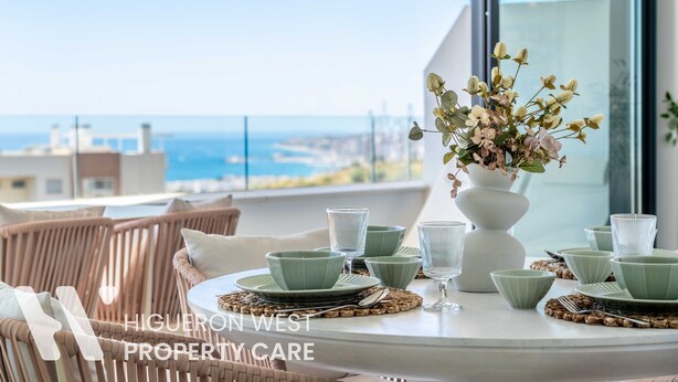 A dining table with green plates and glasses, a white vase with flowers, and wicker chairs.