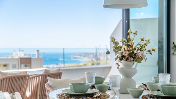 A dining table with green plates and glasses, a white vase with flowers, and wicker chairs.